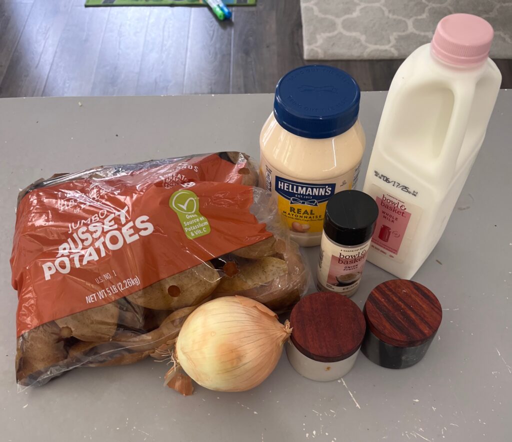 Ingredients for Nan’s creamy potato salad recipe: russet potatoes, onion, mayonnaise, milk, garlic powder, salt, and pepper on a kitchen counter