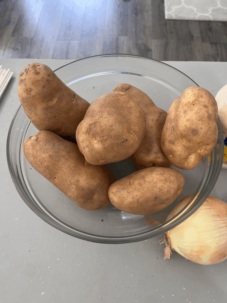 Whole russet potatoes in a glass bowl, ready to be boiled for a creamy homemade potato salad recipe