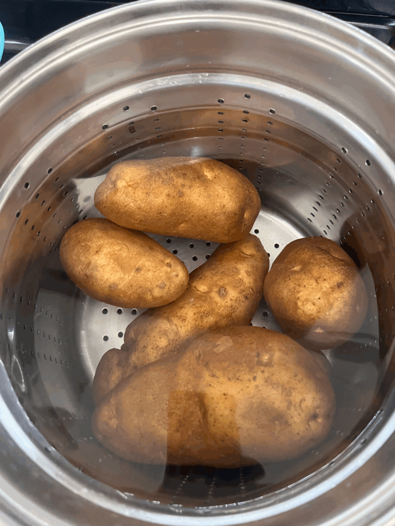 Russet potatoes steaming in a large pot as the first step in making creamy homemade potato salad