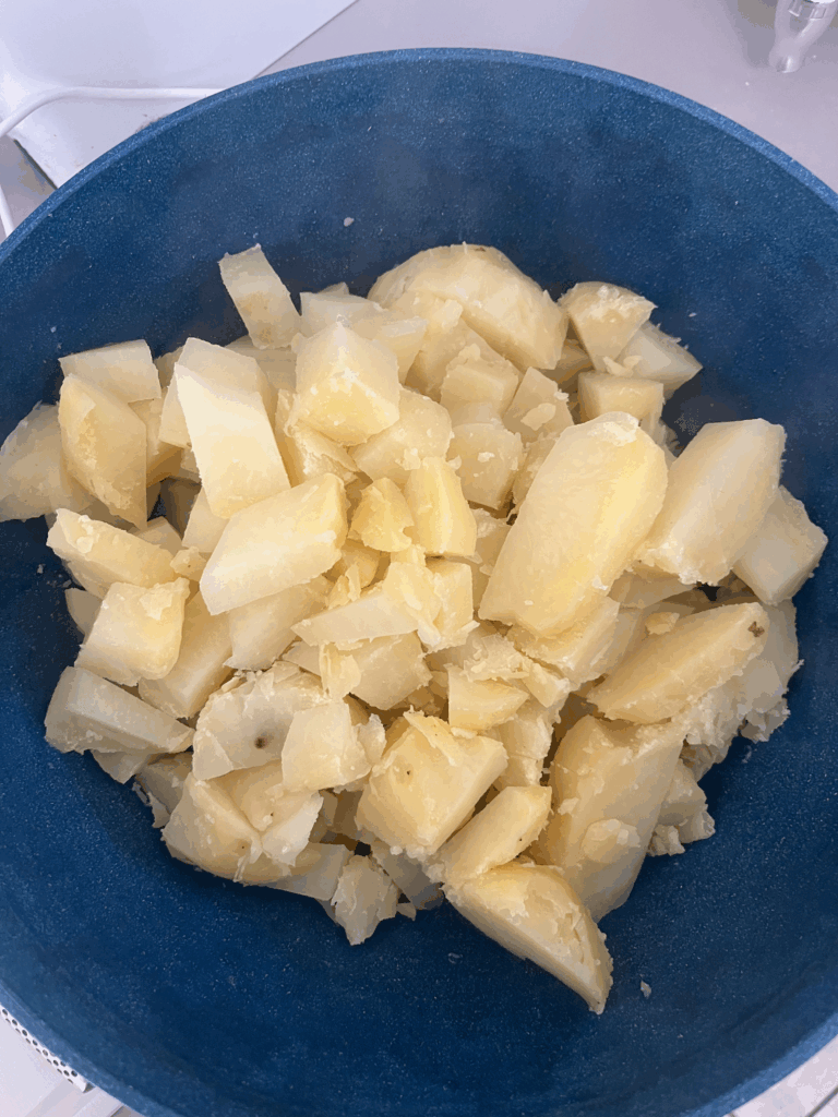 Chopped boiled potatoes in a blue bowl, cooling before mixing into Nan’s creamy potato salad recipe