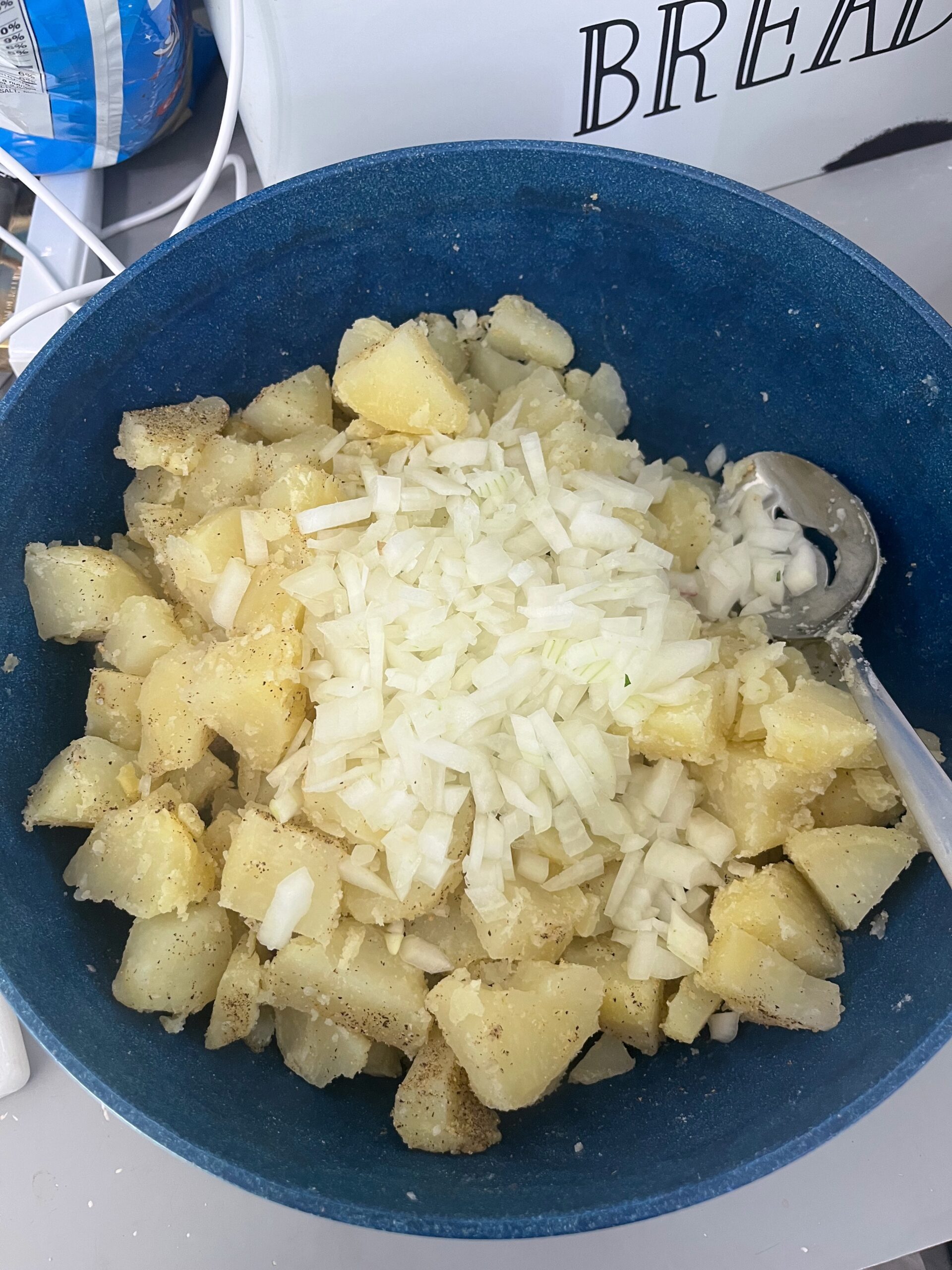 Chopped onions and seasoning added to a bowl of cooked potatoes during prep for creamy homemade potato salad