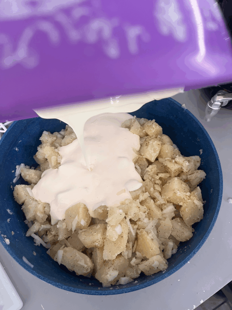 Pouring creamy mayonnaise dressing over seasoned potatoes and onions to make Nan’s famous potato salad