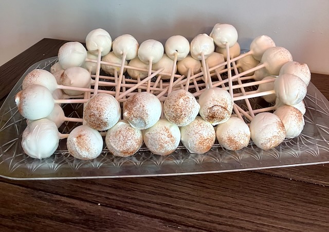 Homemade churro cake pops coated in white chocolate and cinnamon sugar, displayed on a glass platter at a carnival-themed birthday party.