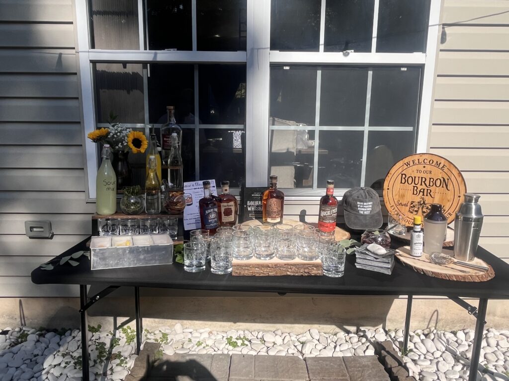 bourbon bar with wood rounds and assorted bottles at backyard party