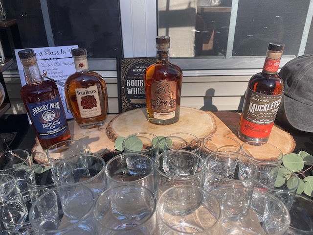 Bourbon bar display at a Bourbon & BBQ 40th birthday party with bottles of Four Roses, Horse Soldier, and other bourbons arranged on wood rounds with etched glasses.