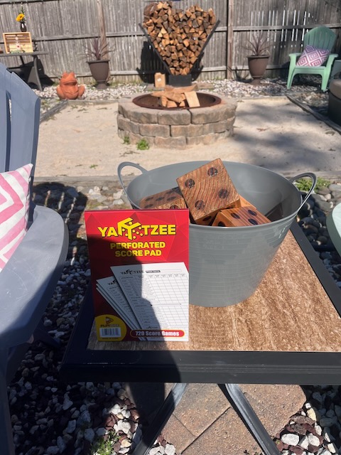 Yard Yahtzee game setup with oversized wooden dice in a bucket and score sheets on a patio table, ready for backyard fun at a 40th birthday Bourbon and BBQ party.