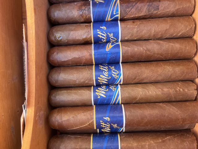 Custom cigars with blue labels reading ‘Matt’s 40th’ displayed in a humidor as part of the cigar bar at a Bourbon and BBQ themed birthday party.