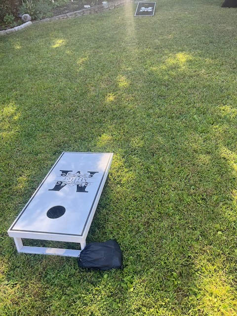 Custom cornhole game set up on the grass for a 40th birthday backyard party, featuring personalized black and white boards with bean bags.