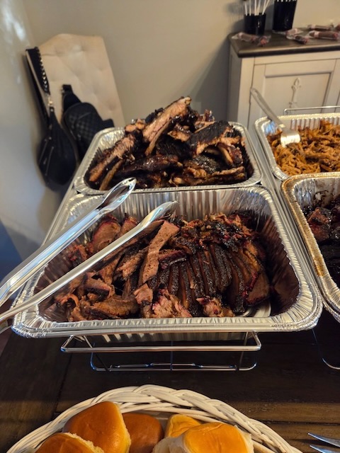 Trays of smoked brisket slices and BBQ ribs at a Bourbon & BBQ 40th birthday party buffet, served alongside pulled pork and slider buns.