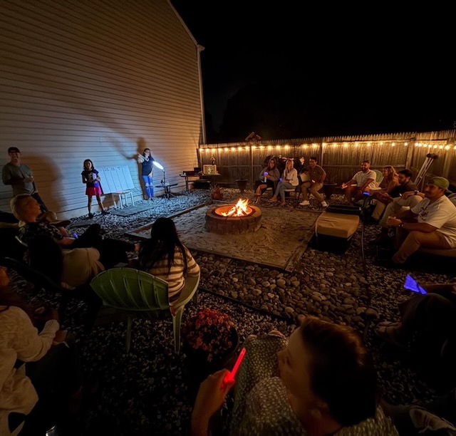 Guests gathered around a glowing backyard fire pit at night, enjoying trivia games and laughter during a 40th birthday Bourbon and BBQ party.