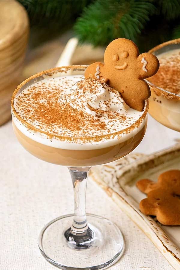 Gingerbread martini cocktail topped with whipped cream, cinnamon, and a gingerbread cookie garnish in a coupe glass.
