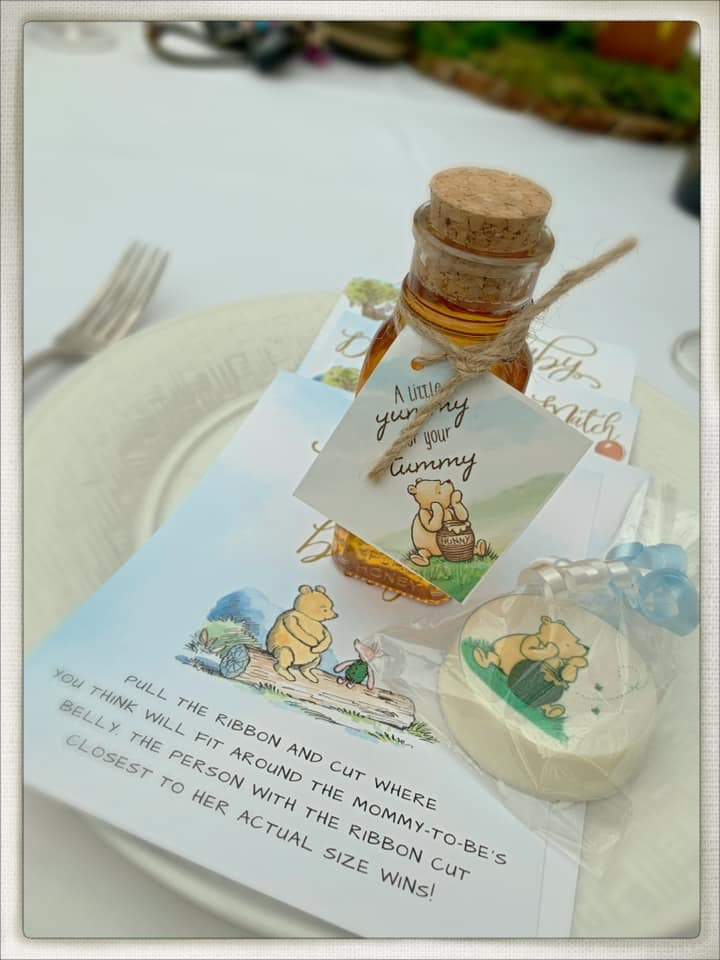 Winnie the Pooh baby sprinkle favor table setting with honey jar favors, themed game card, and chocolate-covered Oreo treats
